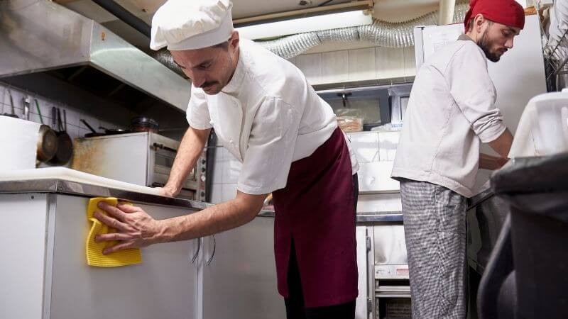 Restaurant employees cleaning the cooking area of a commercial kitchen.