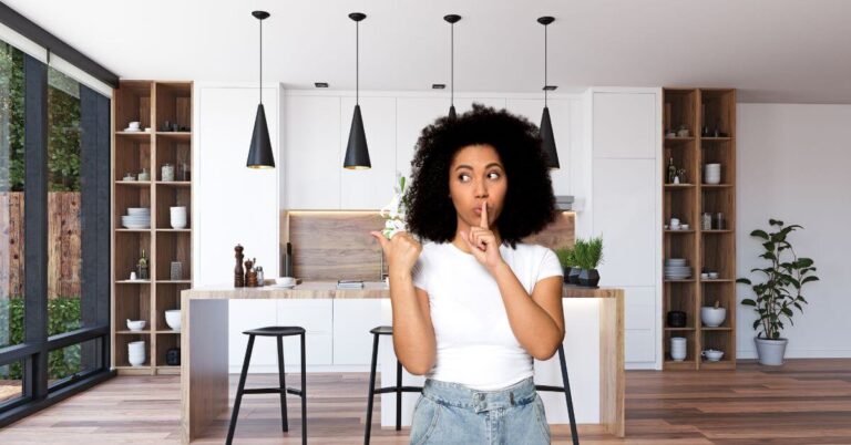 Woman in kitchen with finger up to lips sushing, implying she has a secret.