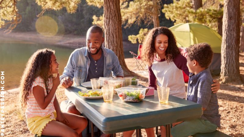 family enjoying a no cooking camping meal of salad next to their tent while camping