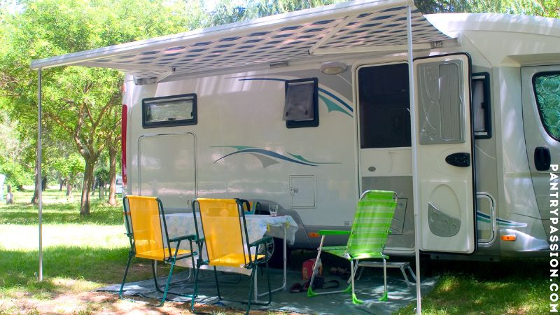 Motorhome with awning opened and lawn chairs set out in a park.