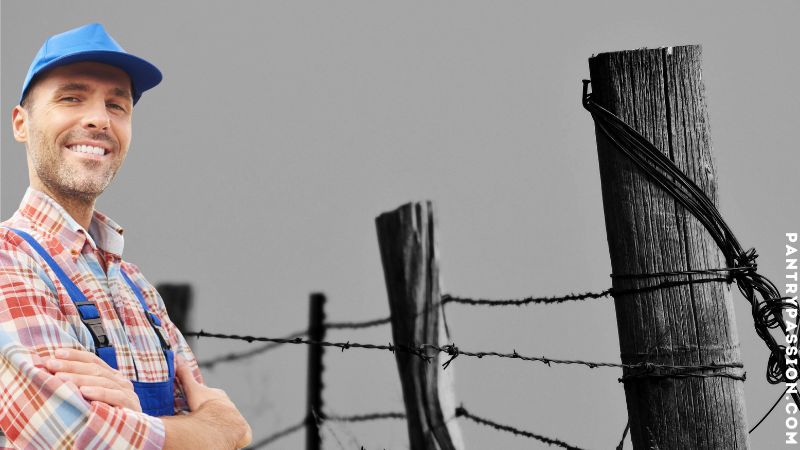 Farmer smiling with arms crossed in foreground' background barbed wire fence.